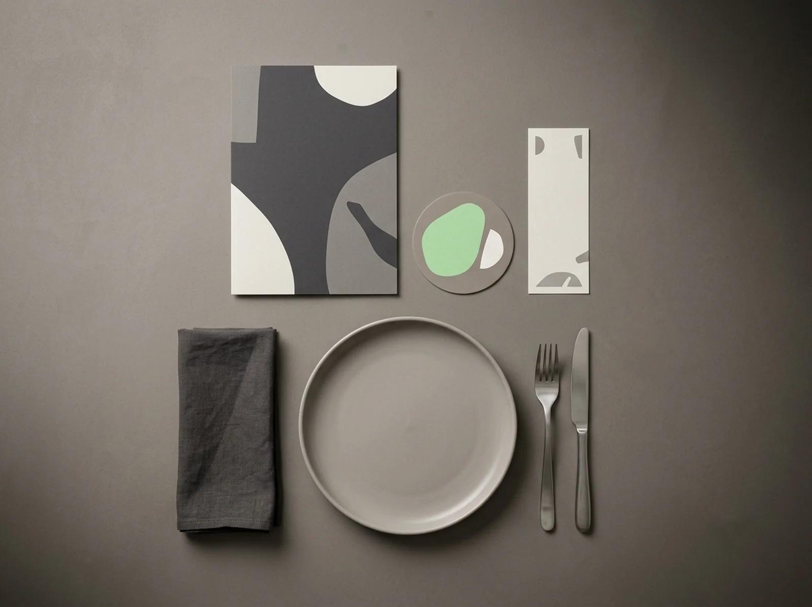 Table dressée moderne : menu, sous-bock, carte, assiette et couverts sur une surface minérale
